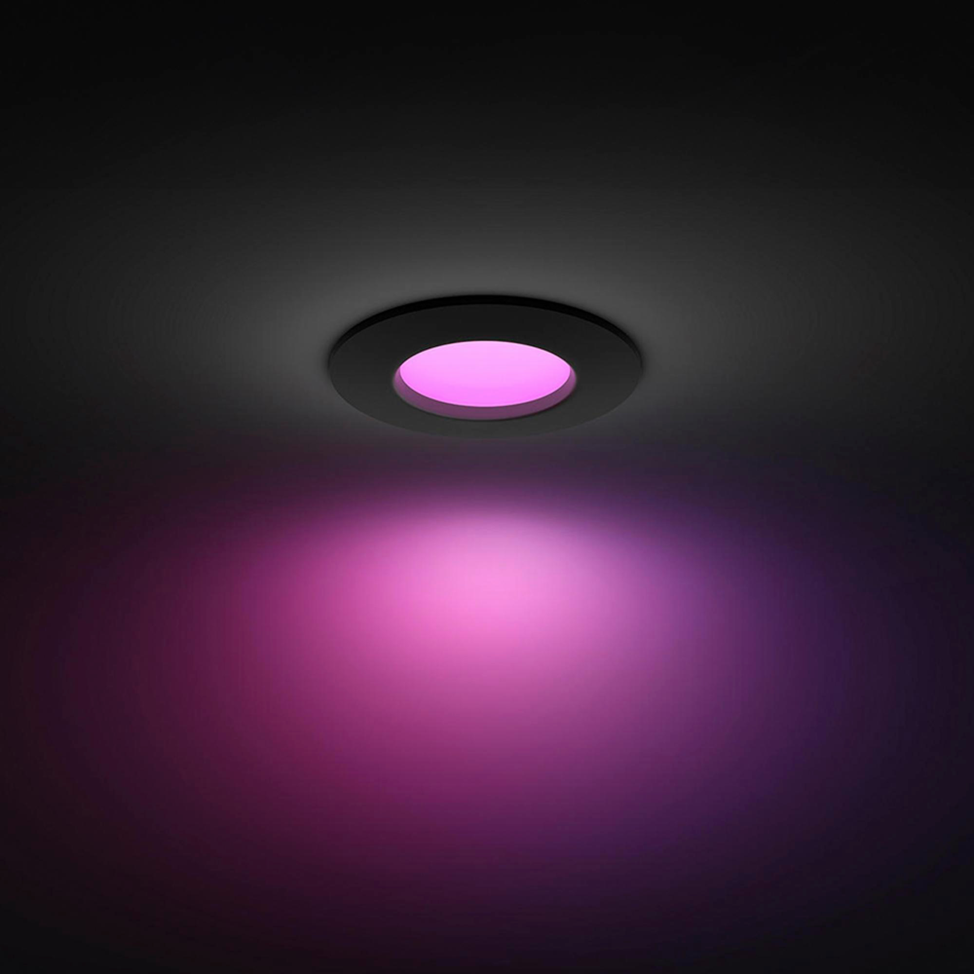 Ein runder, dunkler Deckenstrahler leuchtet pink.
