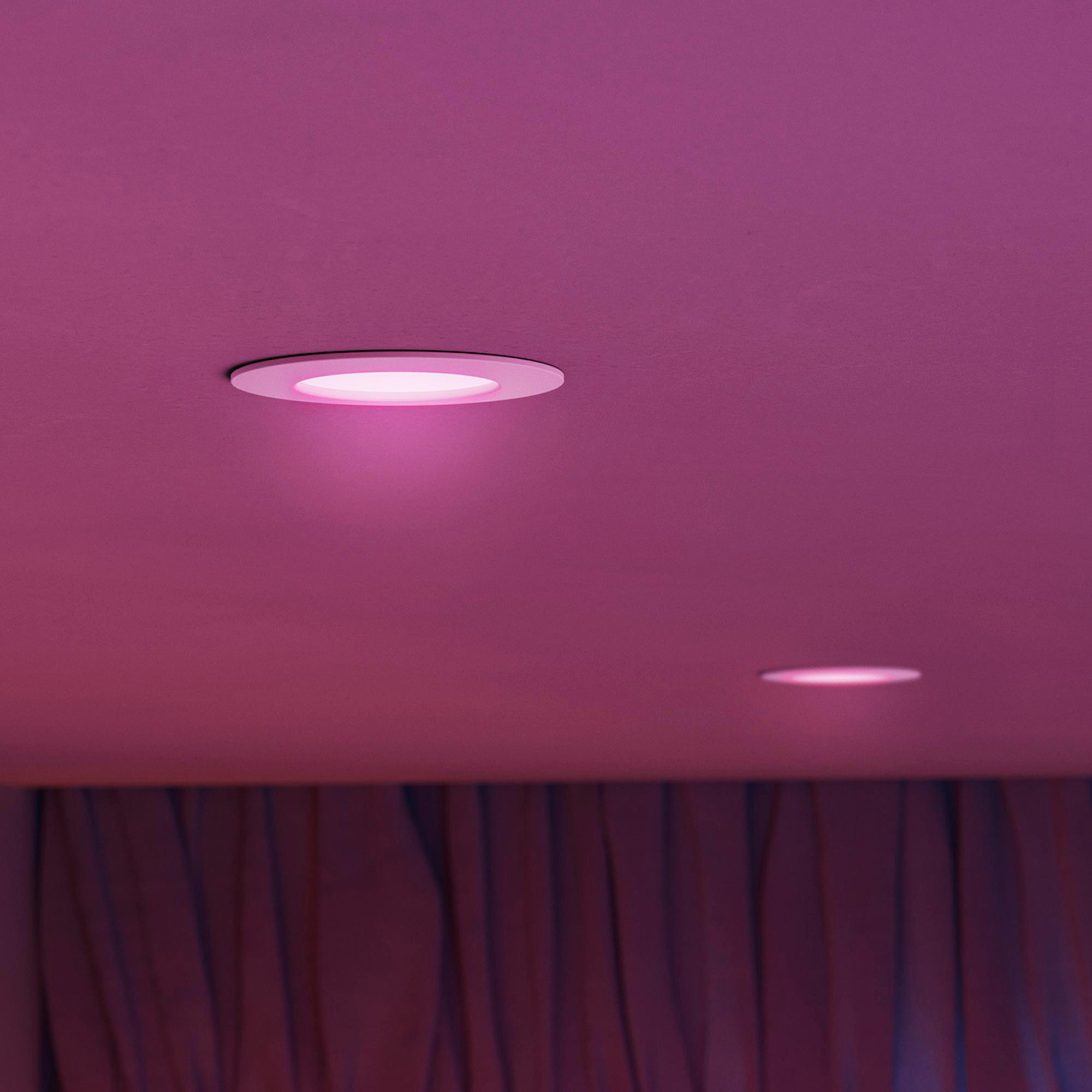 Zwei Einbaustrahler leuchten pink an einer Decke über bordeauxroten Vorhängen.