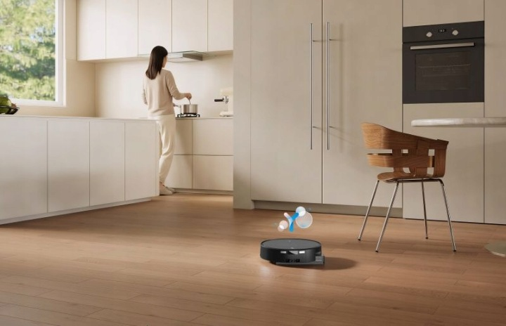 Robot sprzątający czyści podłogę w nowoczesnej kuchni, podczas gdy kobieta gotuje.