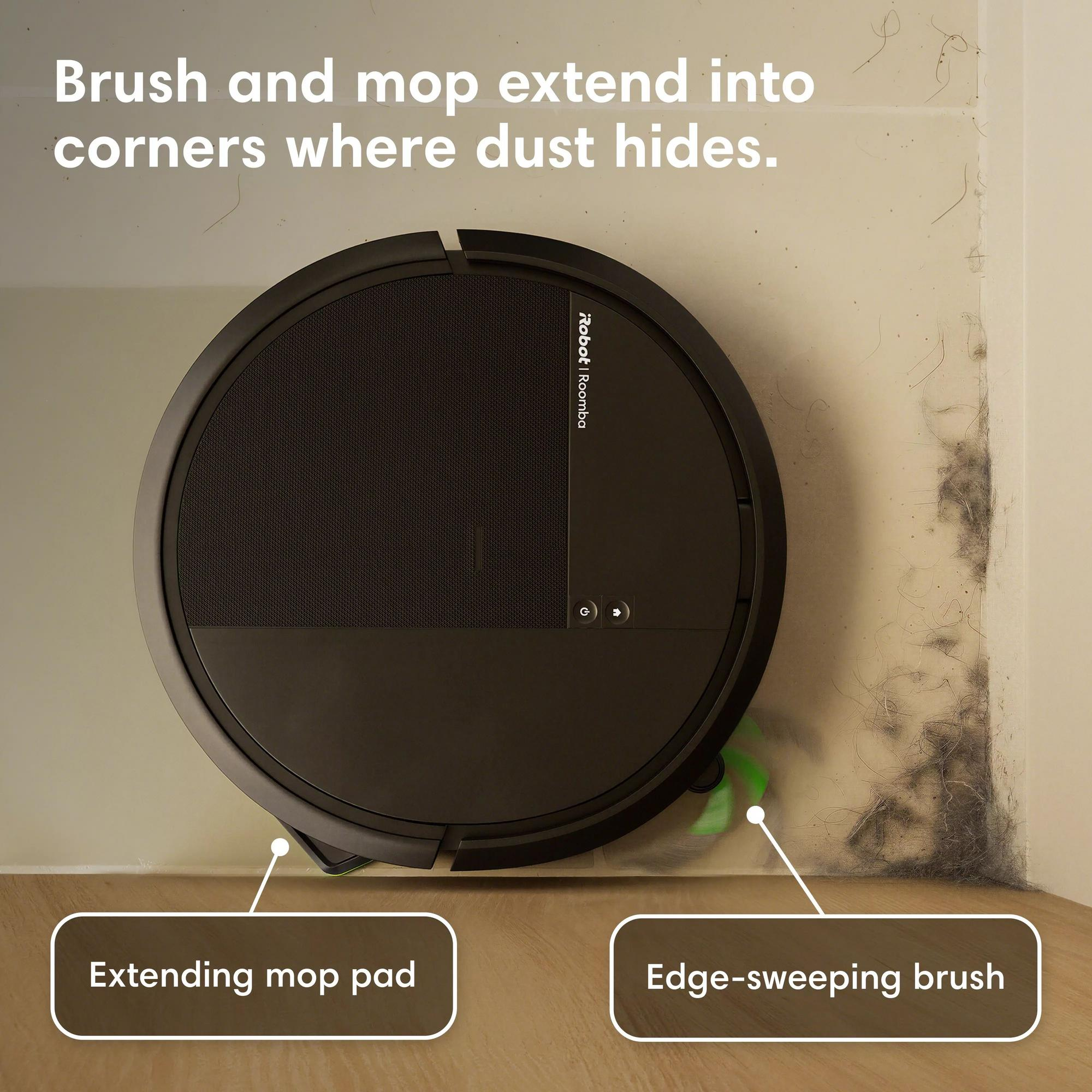 Un aspirateur robot noir nettoyant un coin avec de la poussière et des poils accumulés.