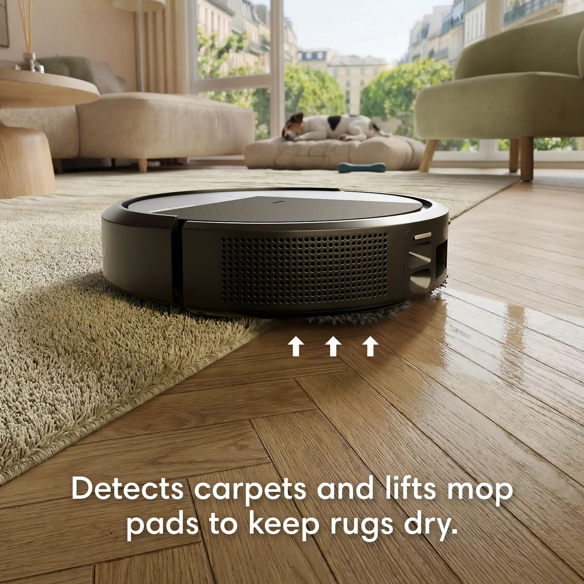 Un robot aspirateur nettoie un parquet près d'un tapis. Un chien dort à l'arrière-plan.