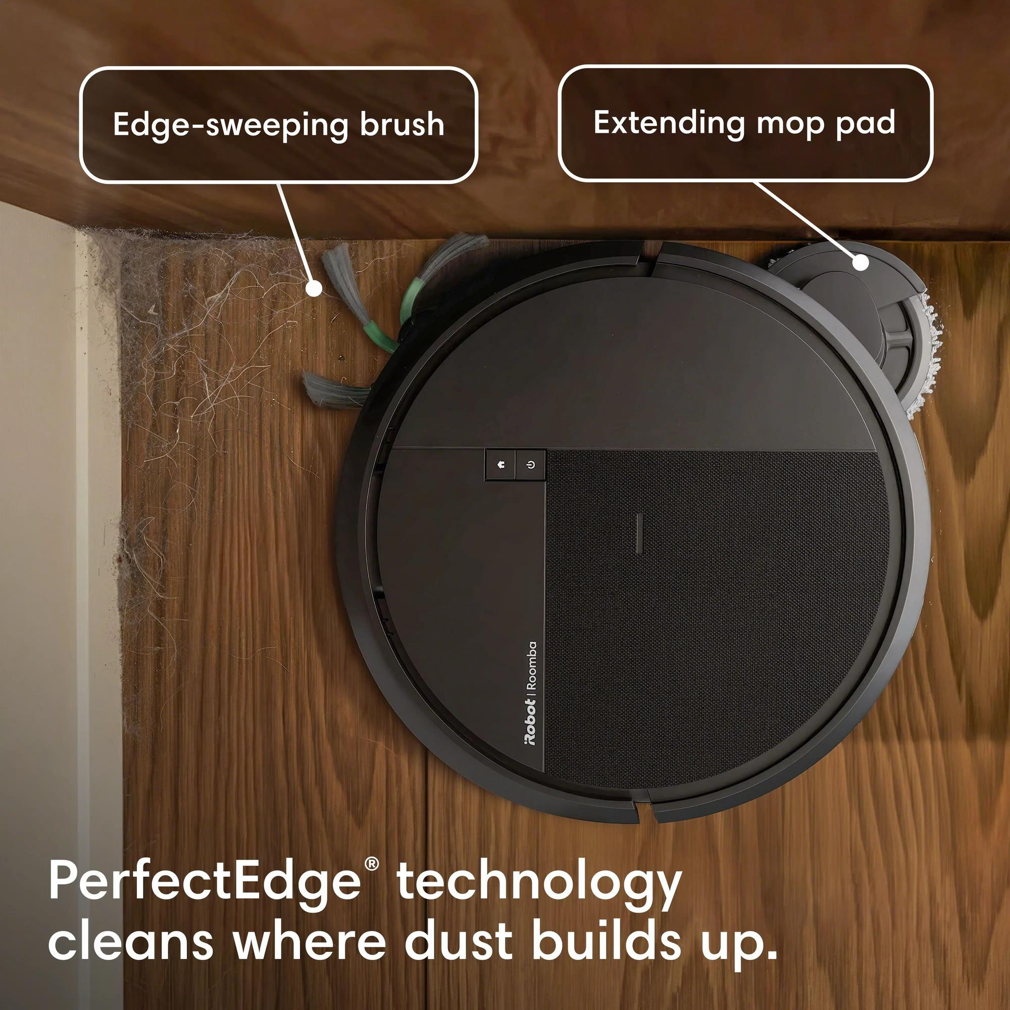 Un aspirateur robot noir nettoie un coin poussiéreux à côté d'un parquet.