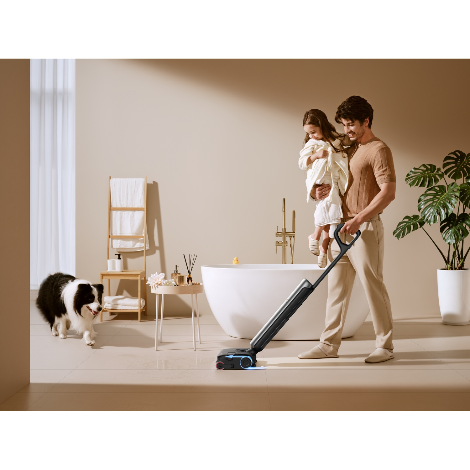 Man holding child cleans bathroom with wet/dry vacuum. Dog stands nearby.
