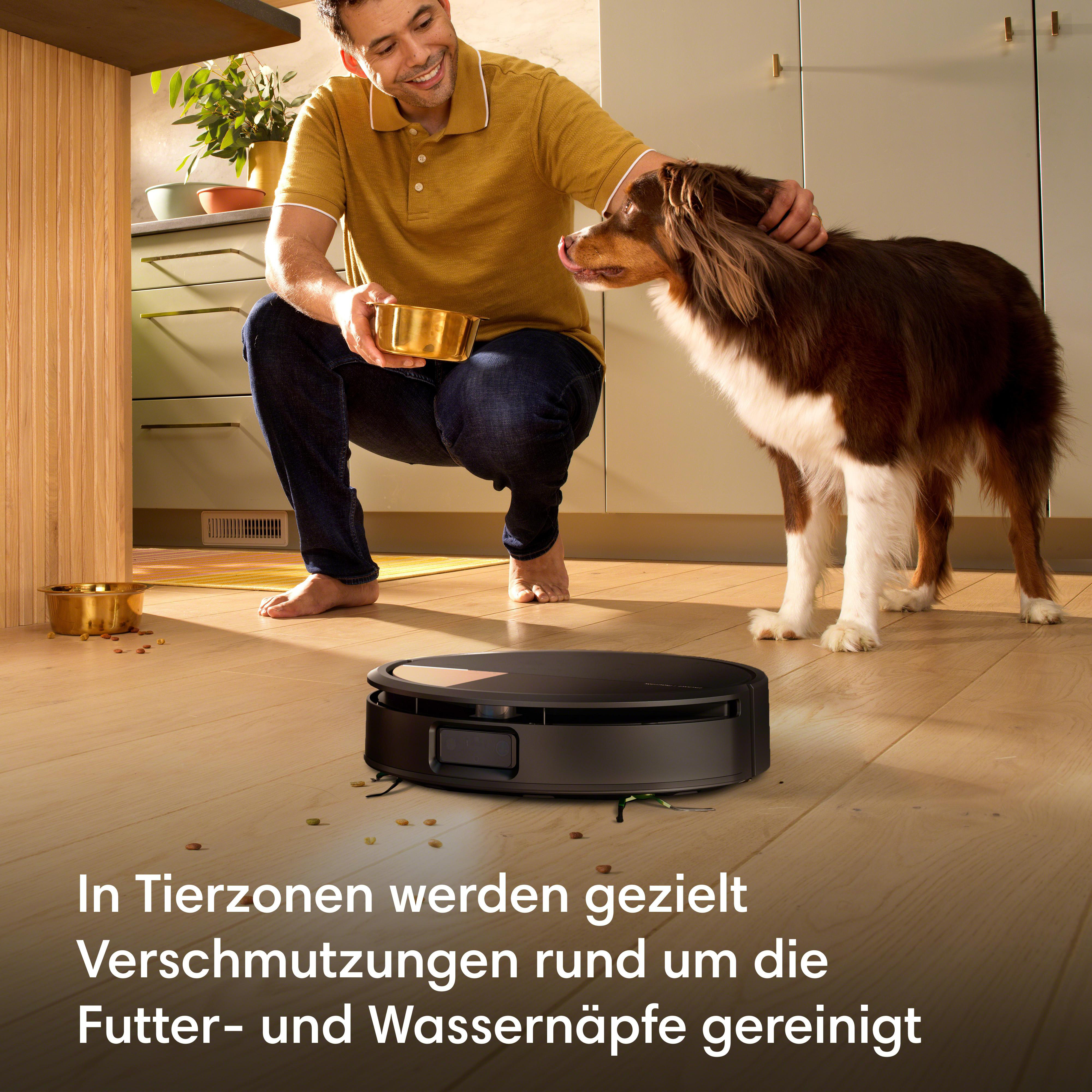 Mann mit Hund und Saugroboter in der Küche, Krümel auf dem Boden.