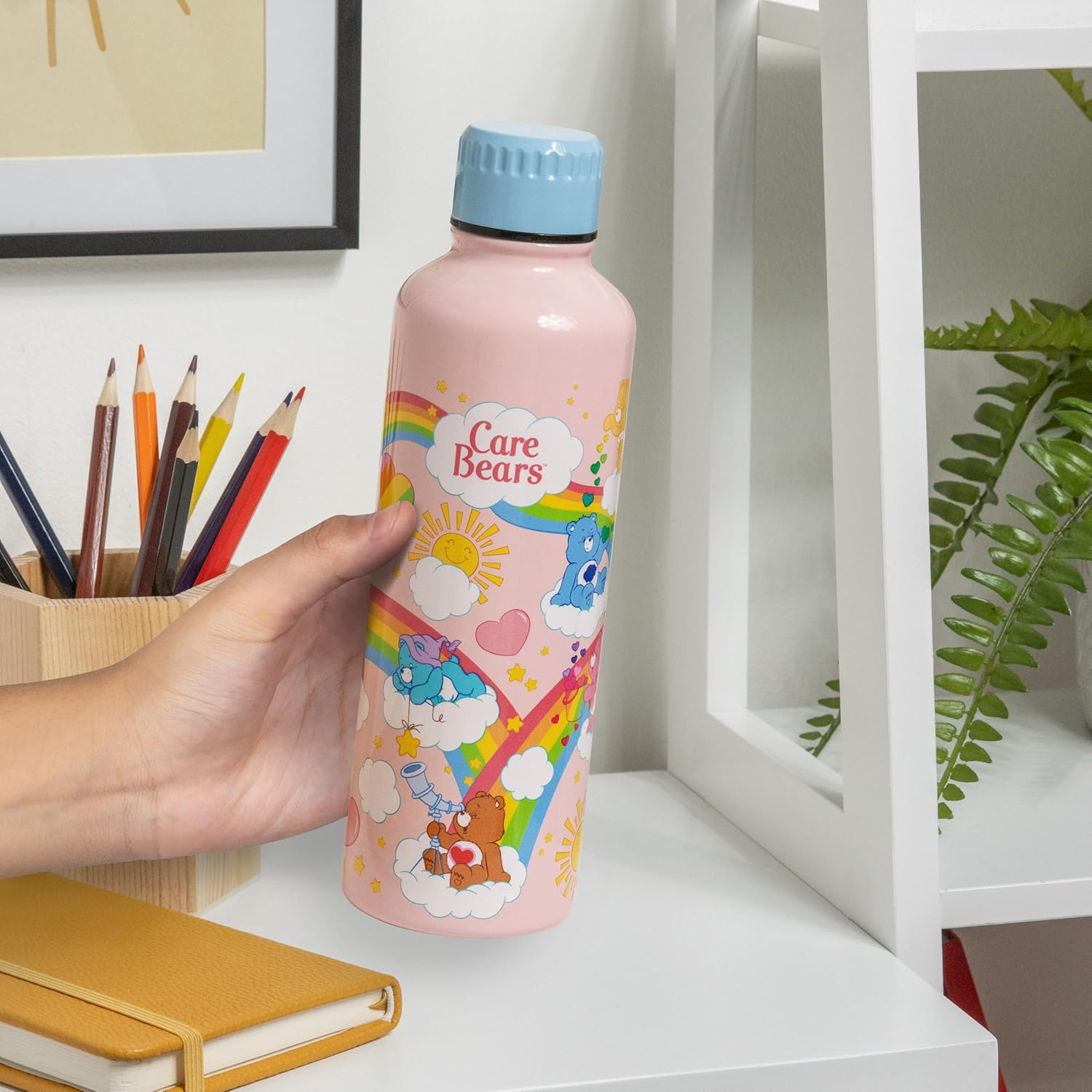 Egy rózsaszín Care Bears kulacs, amelyet egy kéz tart, hátul ceruzákkal.