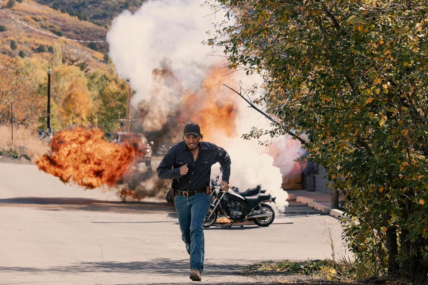 Ein Mann rennt vor einer Explosion und Rauch davon, ein Motorrad steht daneben.
