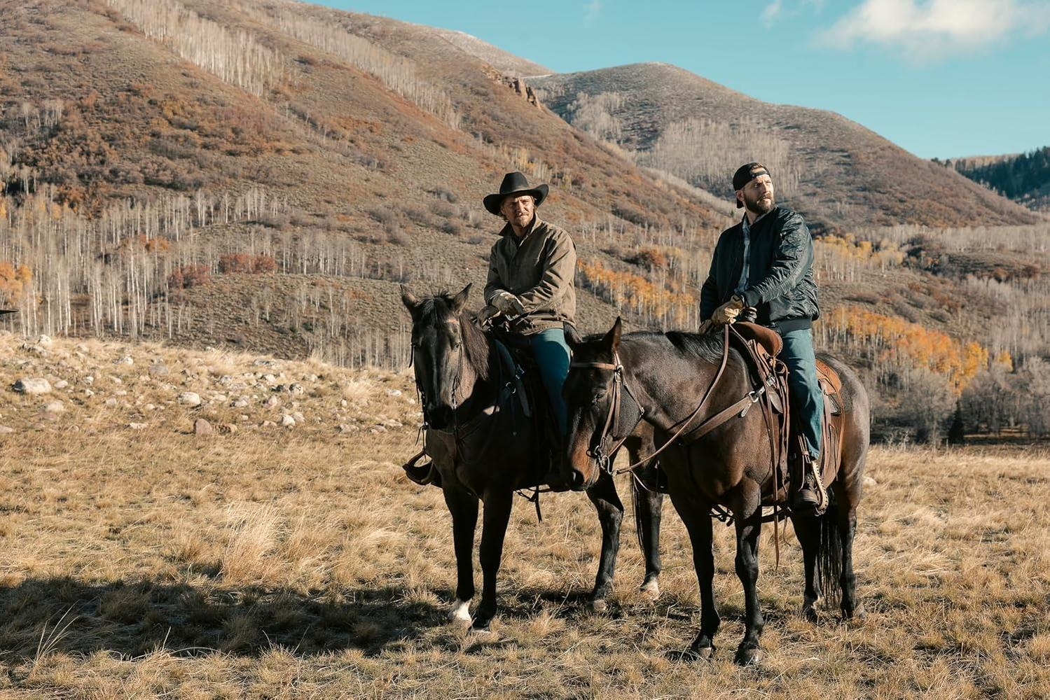 Zwei Männer reiten auf Pferden in einer trockenen Landschaft mit Bergen.