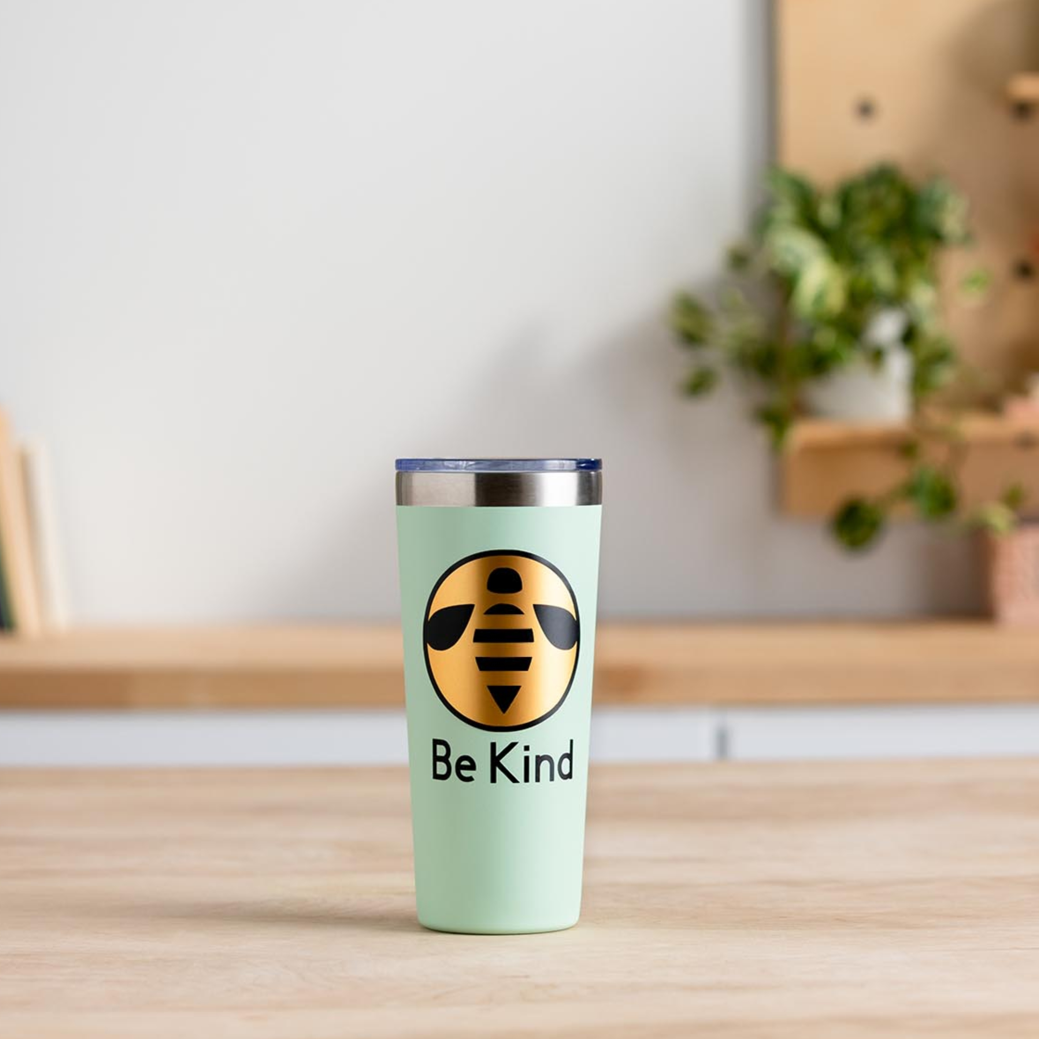 Arı logosu ve "Be Kind" yazılı açık yeşil bir kupa.
