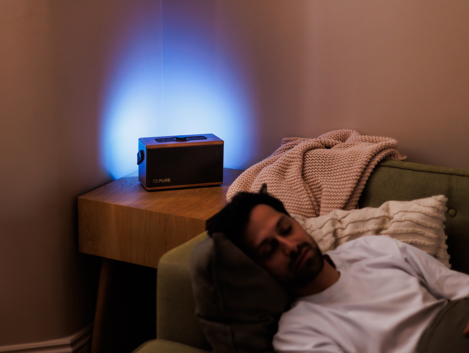 Mann schläft auf einer Couch neben einem Lautsprecher mit blauem Licht.
