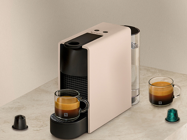 Una máquina Nespresso color crema con dos tazas de espresso y cápsulas de café.