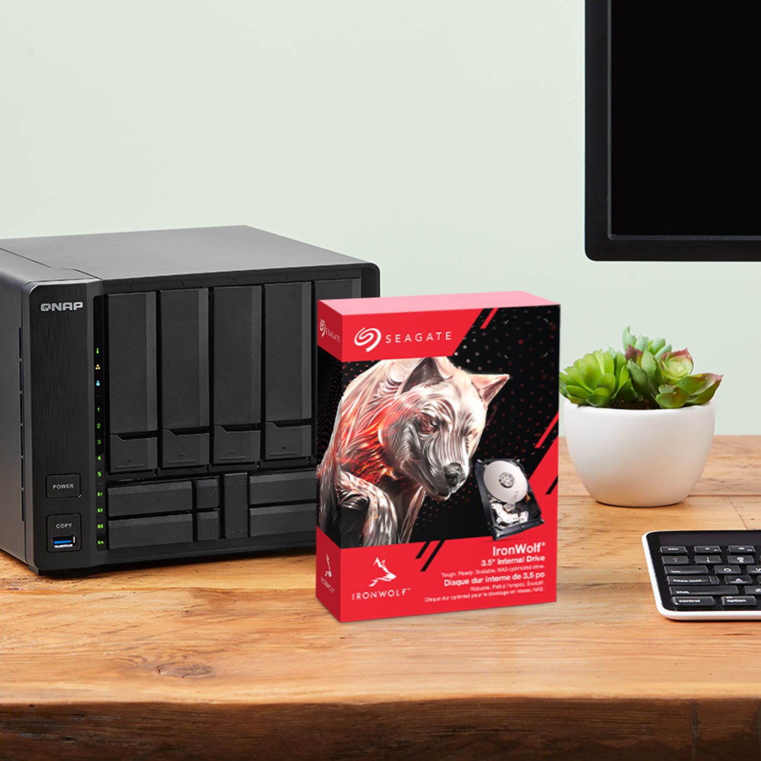 NAS QNAP, boîte de disque Seagate IronWolf, clavier et plante sur un bureau en bois.
