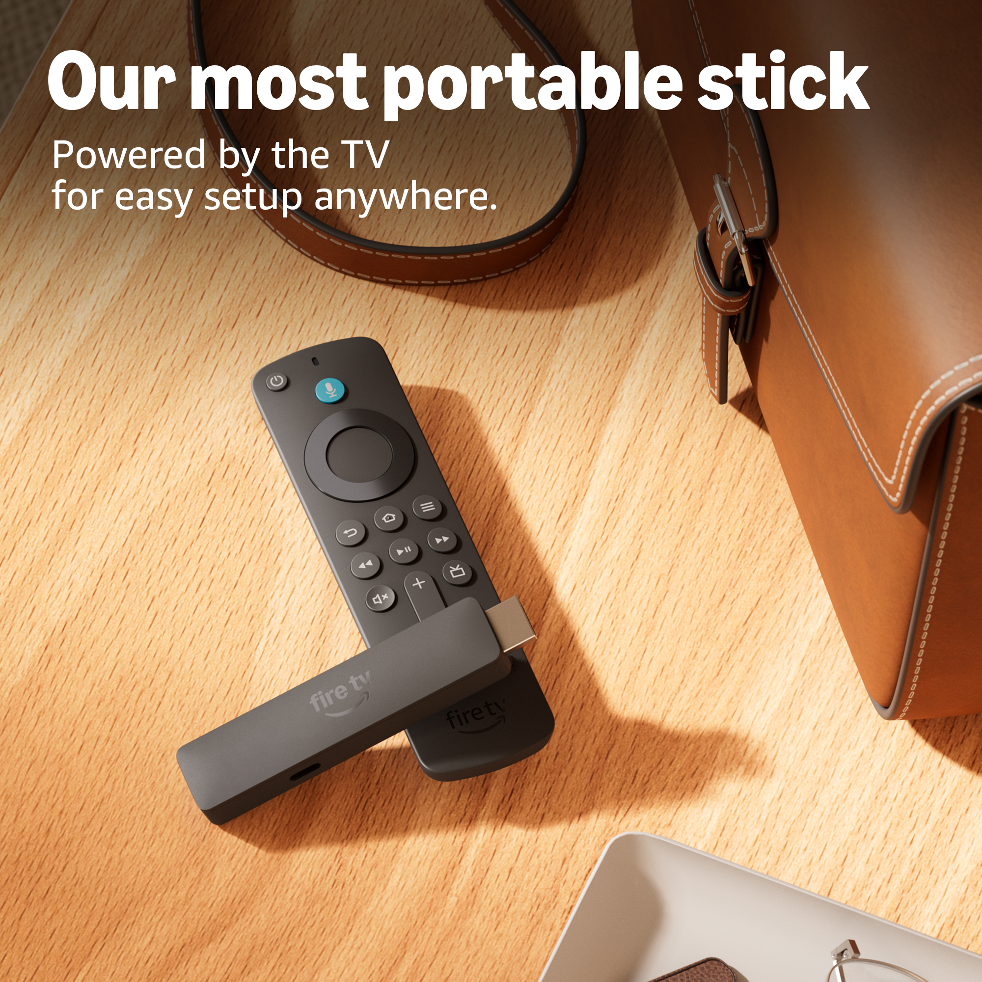 Un Fire TV stick e telecomando neri su tavolo di legno, accanto a borsa in pelle marrone.