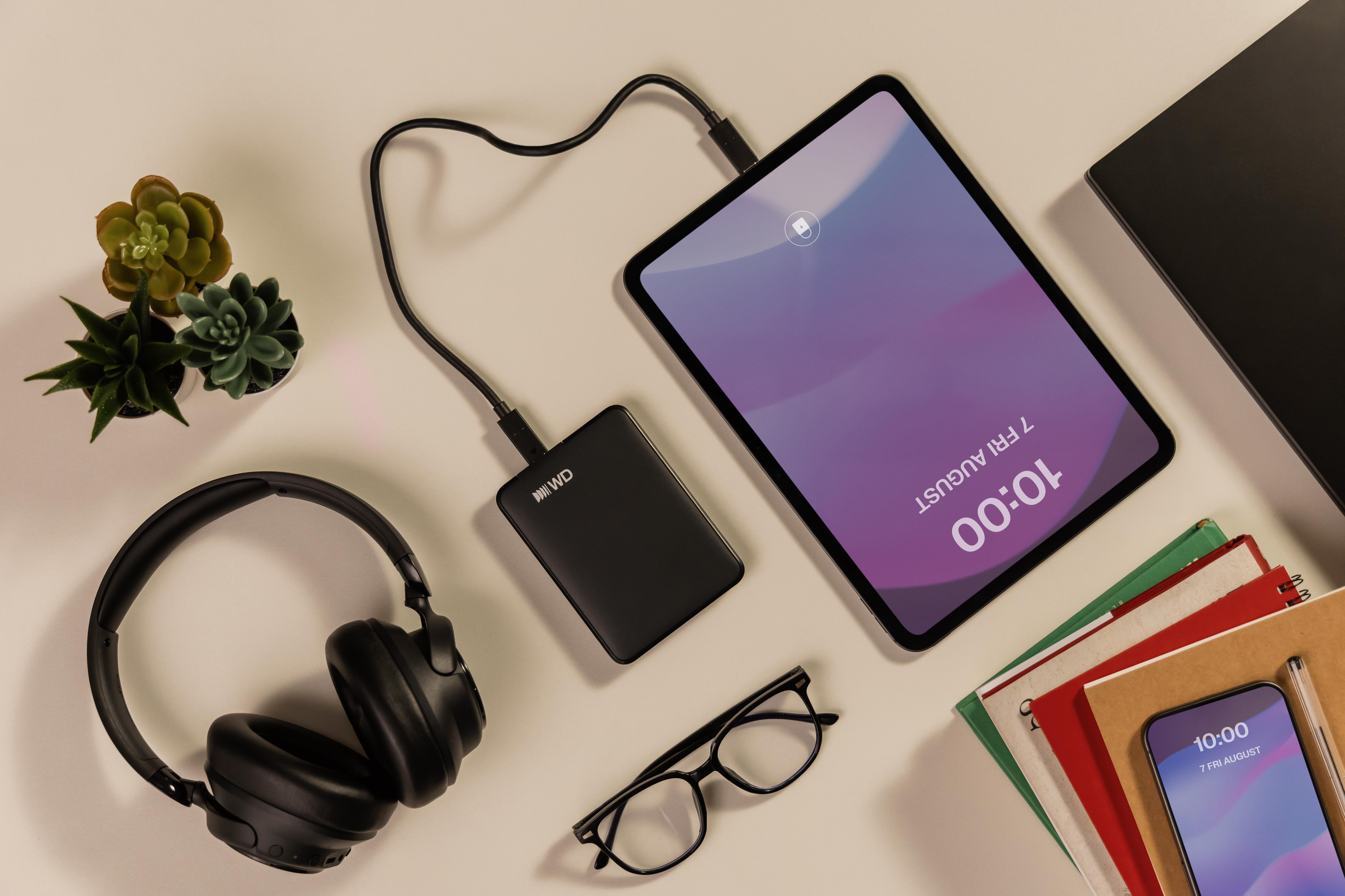 Schwarze Kopfhörer, externe Festplatte und Tablet auf hellem Hintergrund.