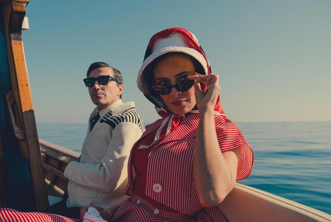 Ein Mann und eine Frau in Vintage-Kleidung auf einem Boot mit blauem Himmel und Meer.