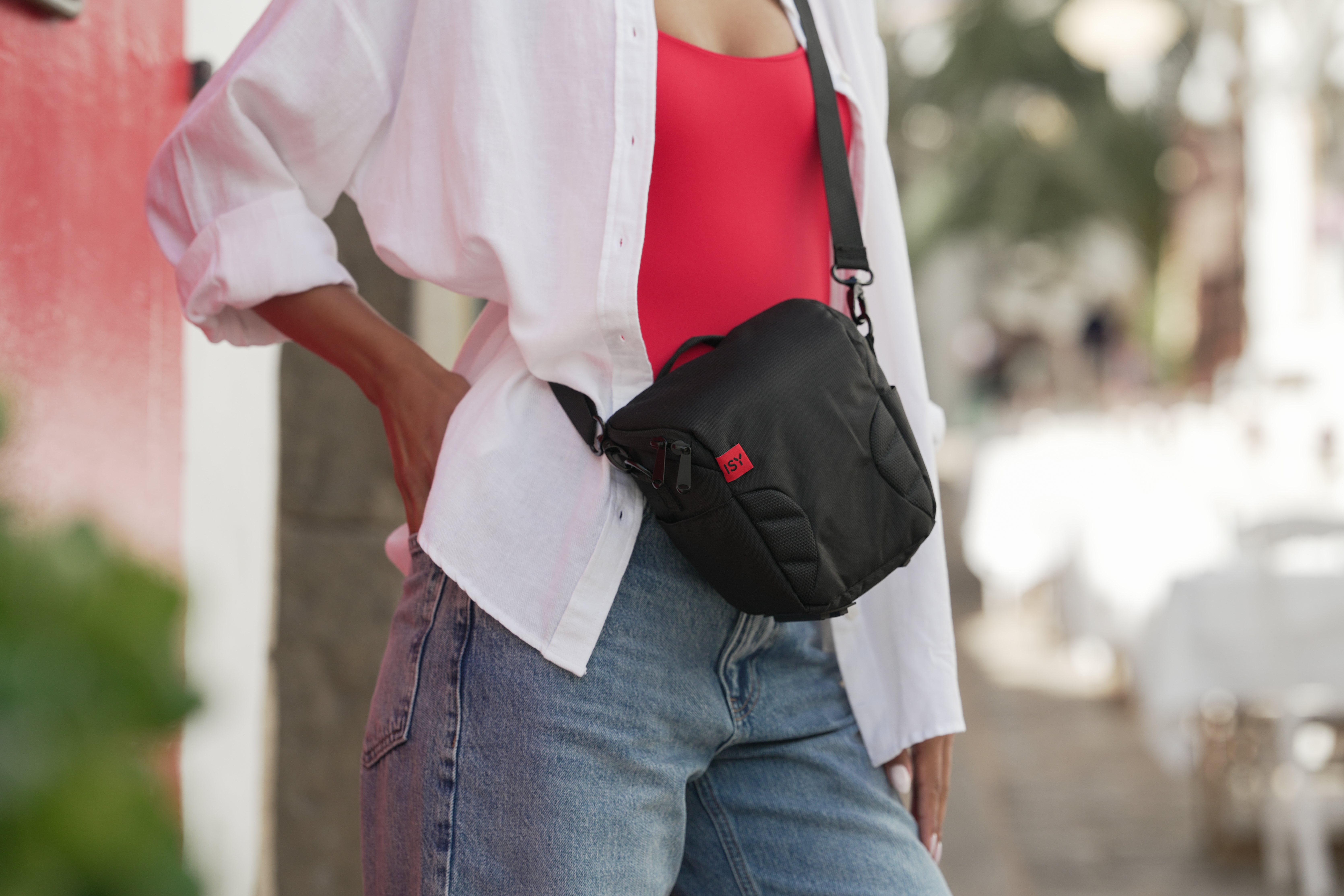 Frau im roten Oberteil, weißem Hemd und Jeans trägt schwarze Tasche.