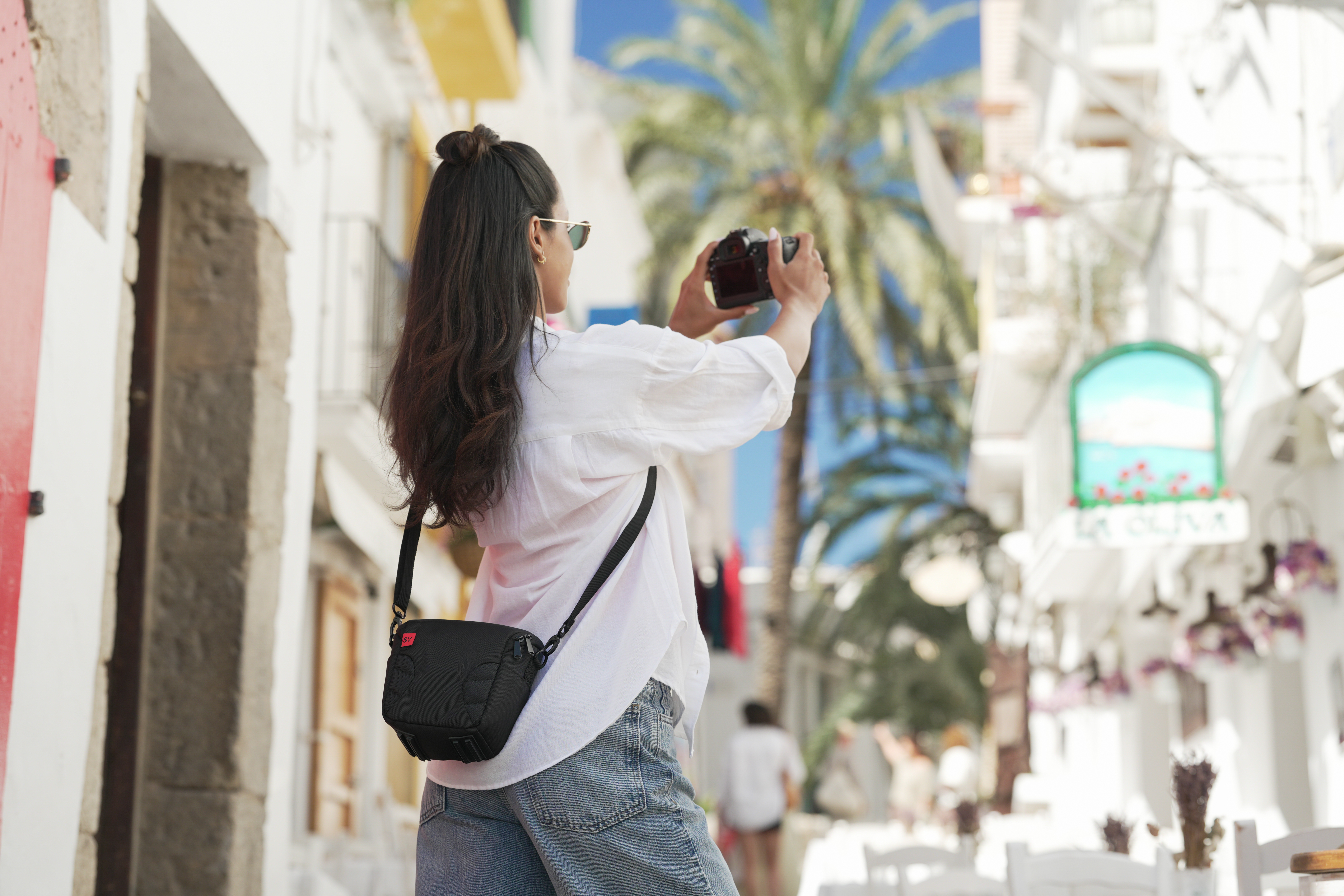Eine Frau mit Kamera fotografiert auf einer sonnigen Straße mit Palmen.