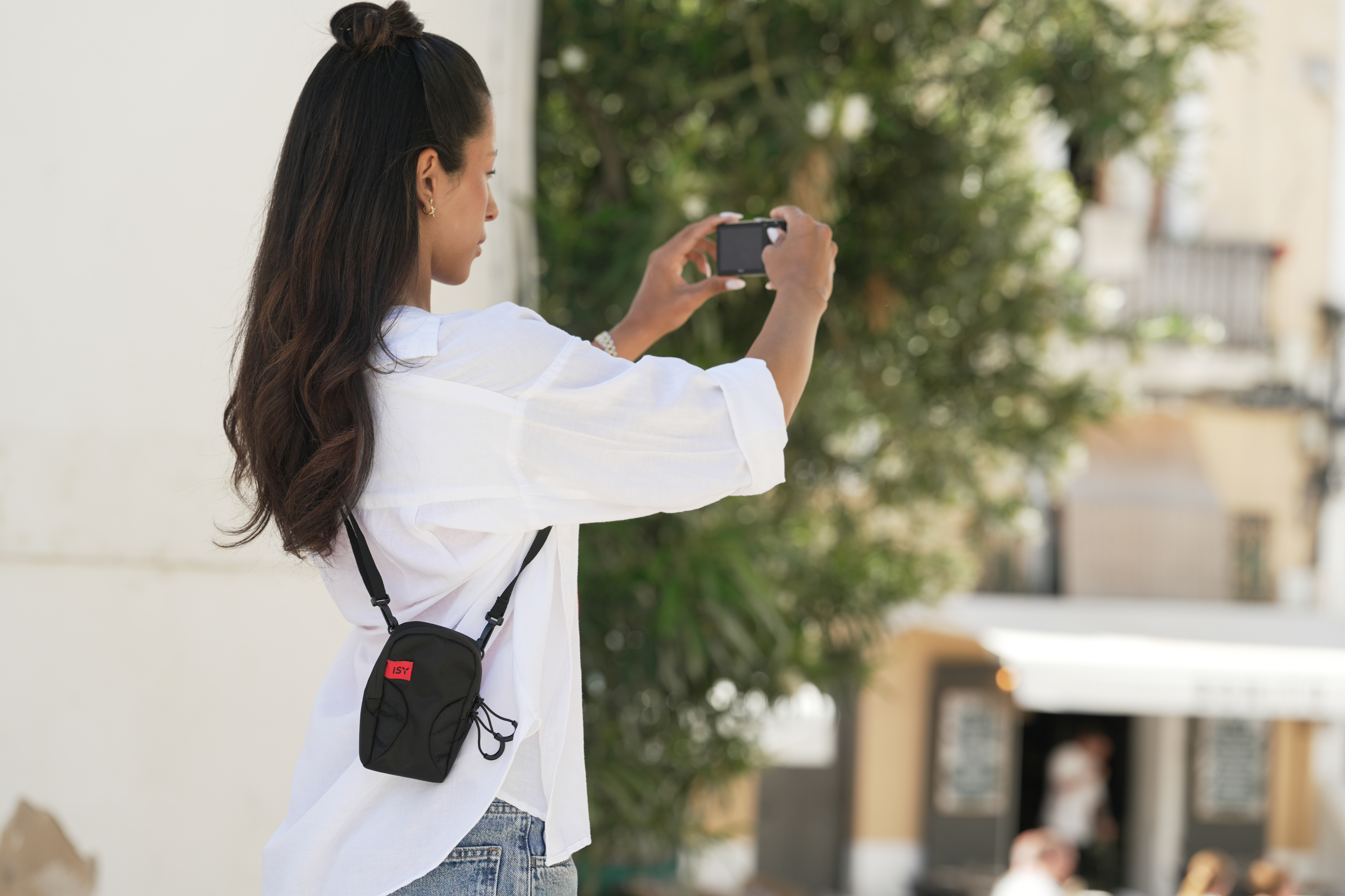 Eine Frau mit dunklem Haar fotografiert mit einer Kamera in einer Straße.