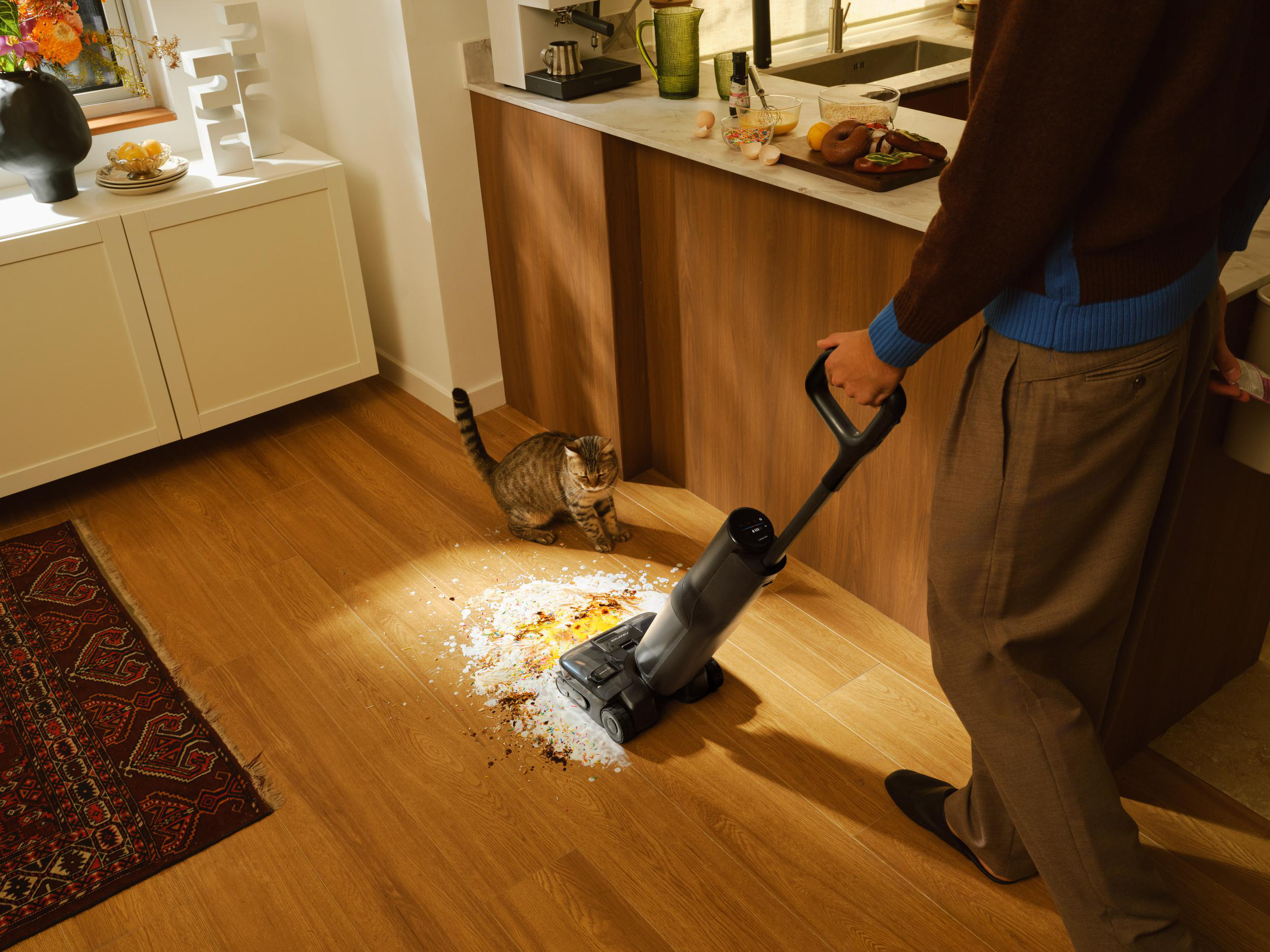Eine Katze beobachtet, wie ein Mann mit einem Staubsauger einen verschütteten Haufen reinigt.