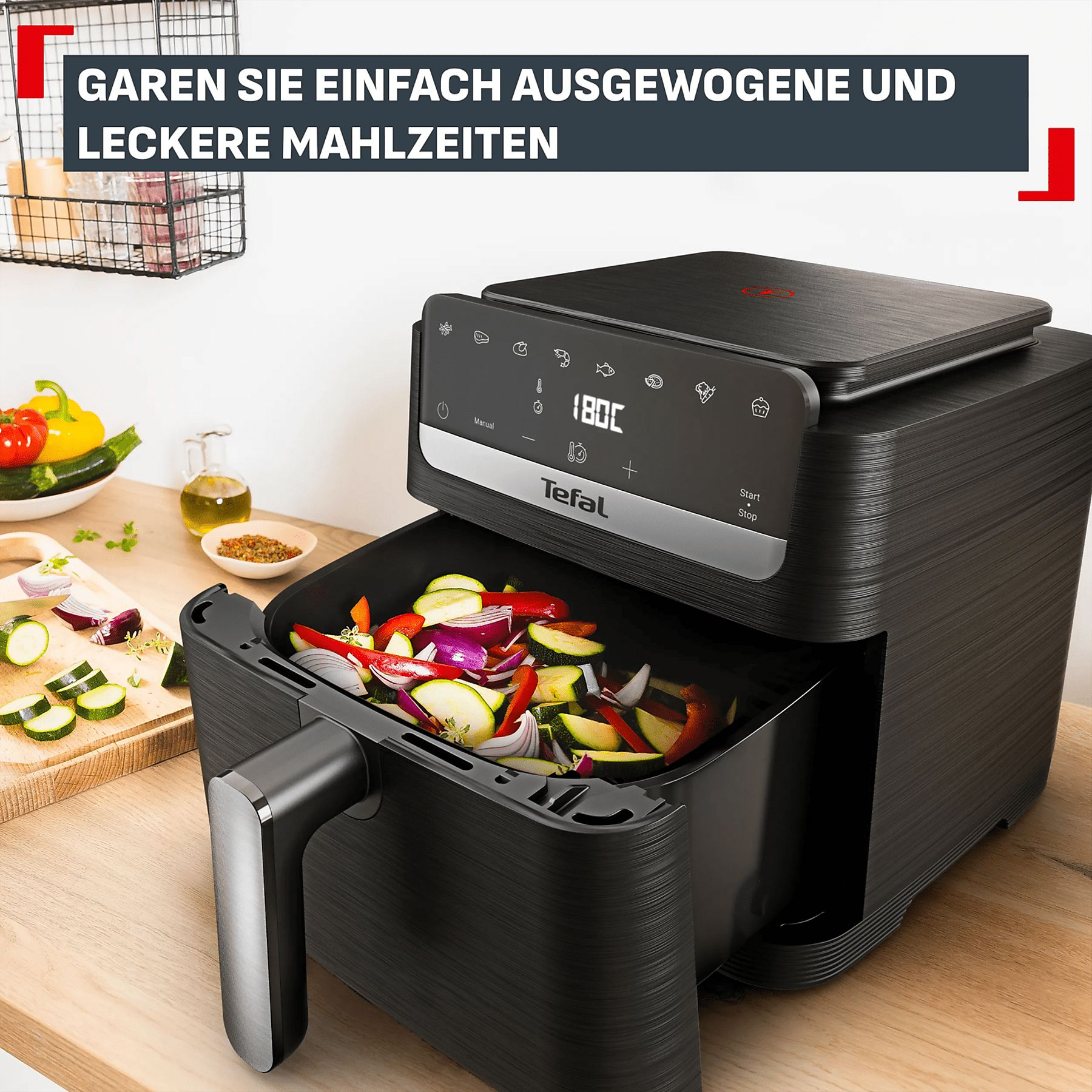Friteuse à air noire remplie de légumes, avec des légumes coupés à proximité.