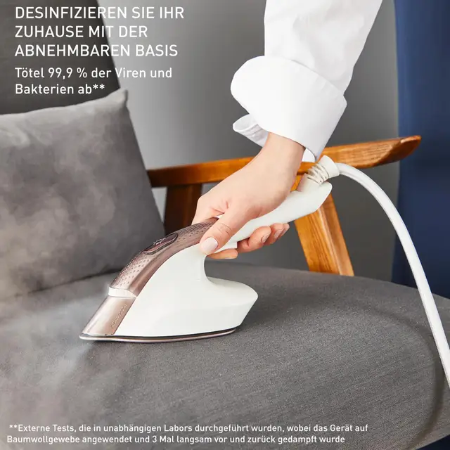 Eine Hand benutzt einen Dampfglätter, um ein graues Sofa zu desinfizieren.