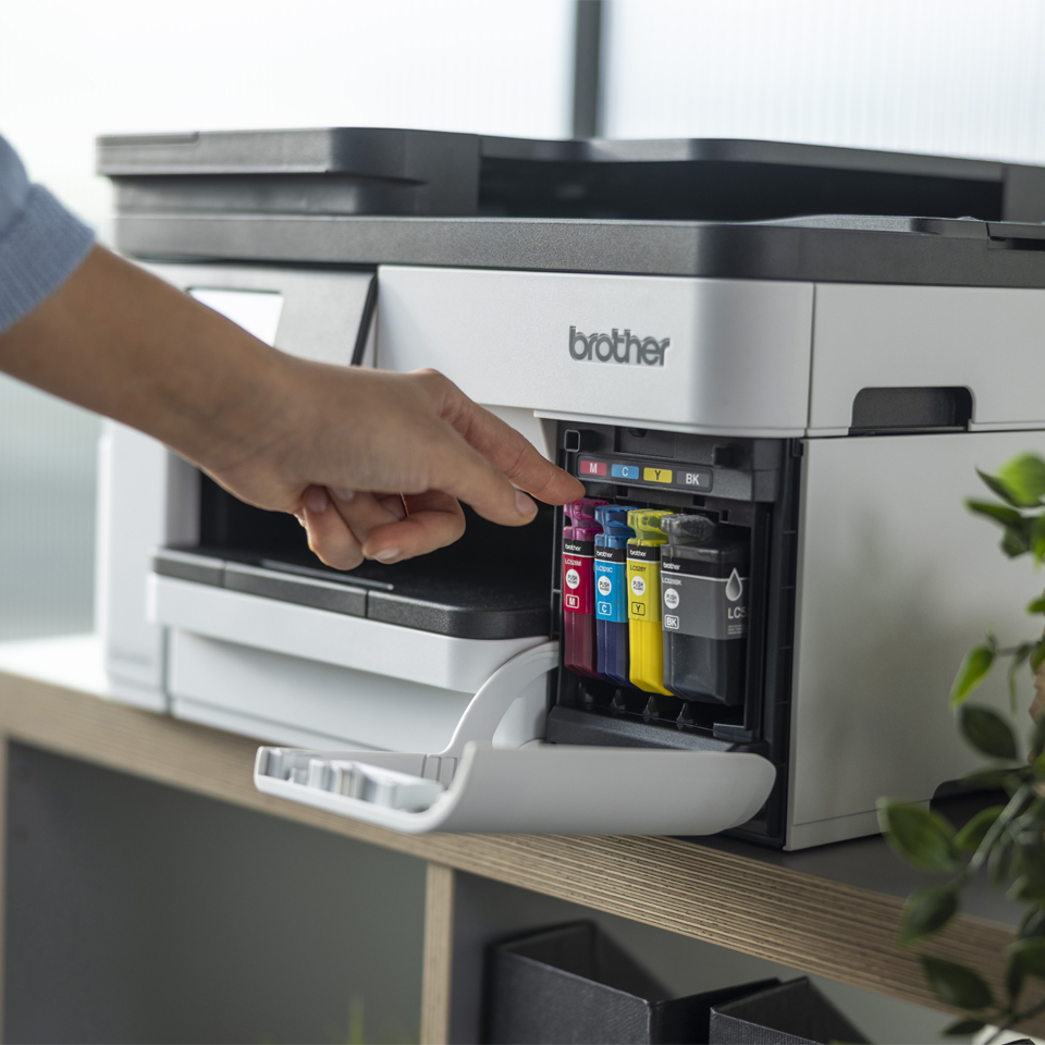 Une main remplace une cartouche d'encre magenta dans une imprimante Brother.