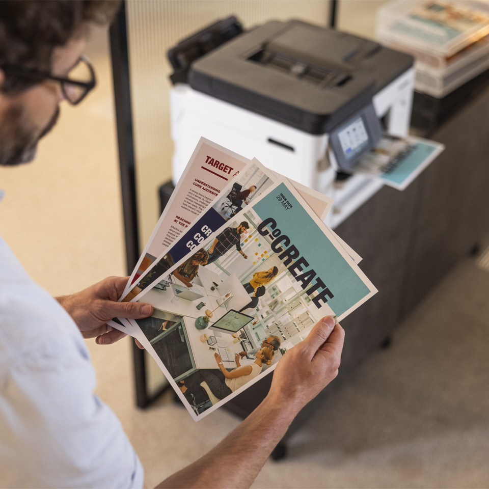 Homme tenant des brochures avec des scènes de bureau. Imprimante en arrière-plan.