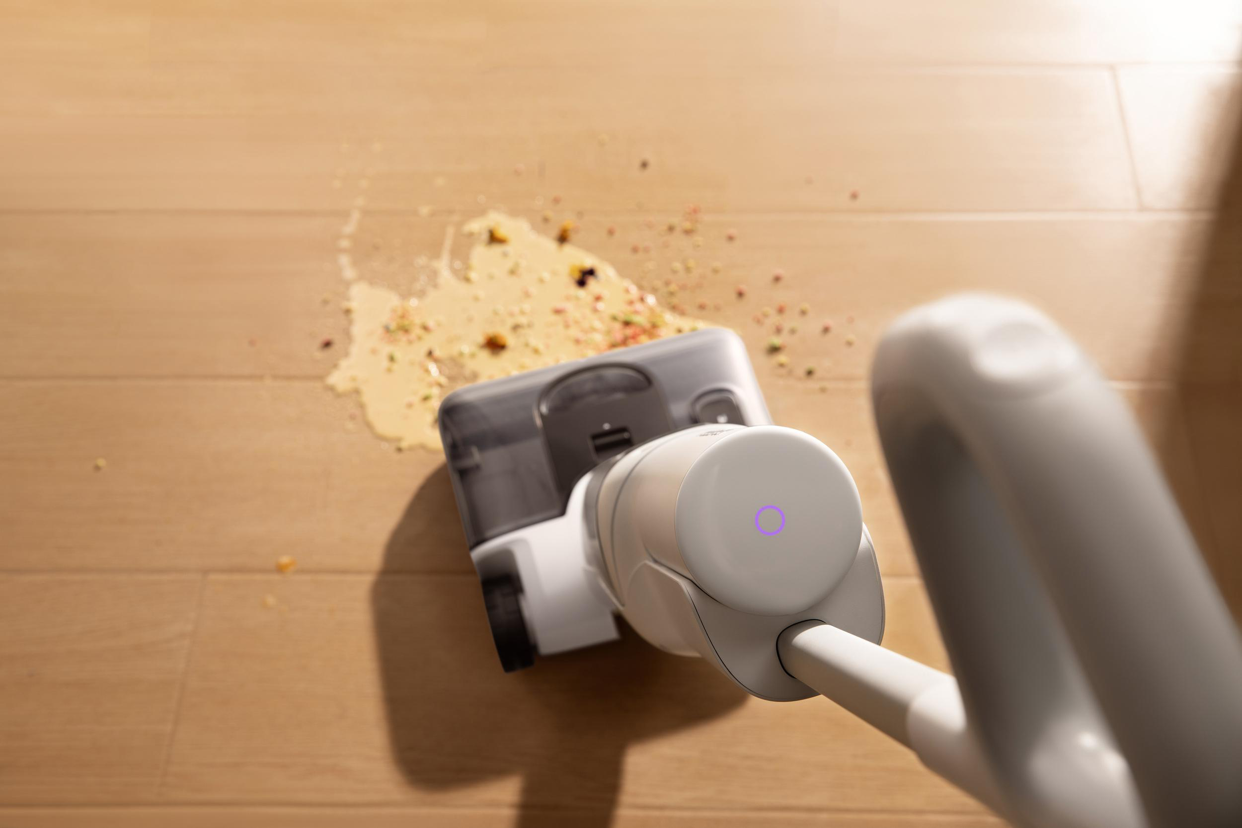 Ein weißer Staubsauger reinigt verschüttetes Essen auf einem Holzboden.