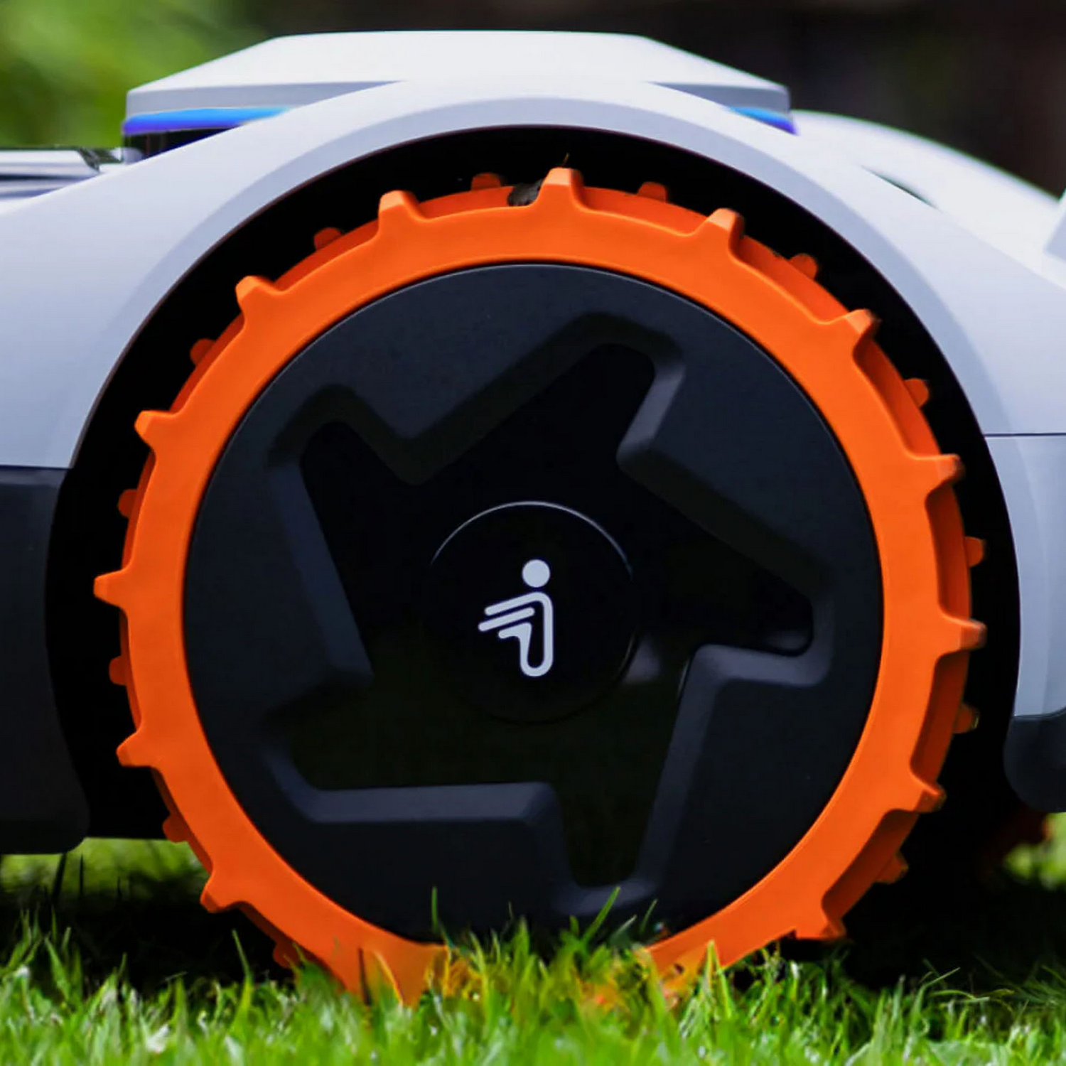 Un robot cortacésped blanco con rueda naranja sobre césped verde.