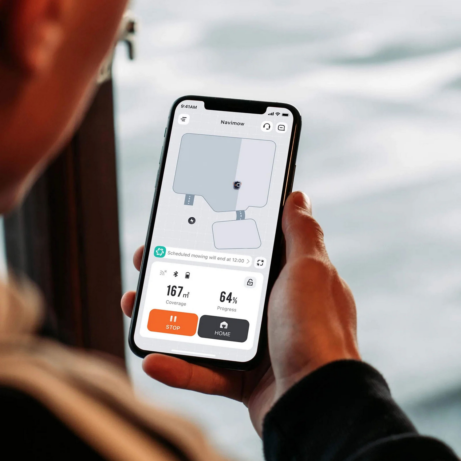 Una persona sostiene un teléfono inteligente que muestra una aplicación de cortacésped con mapa, cobertura y progreso.