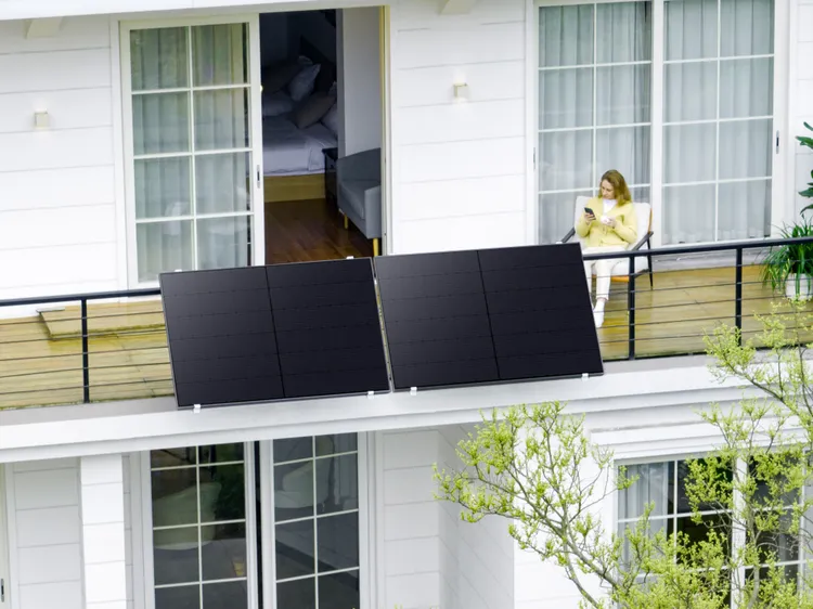 Paneles solares negros en un balcón con una mujer con top amarillo usando su teléfono.