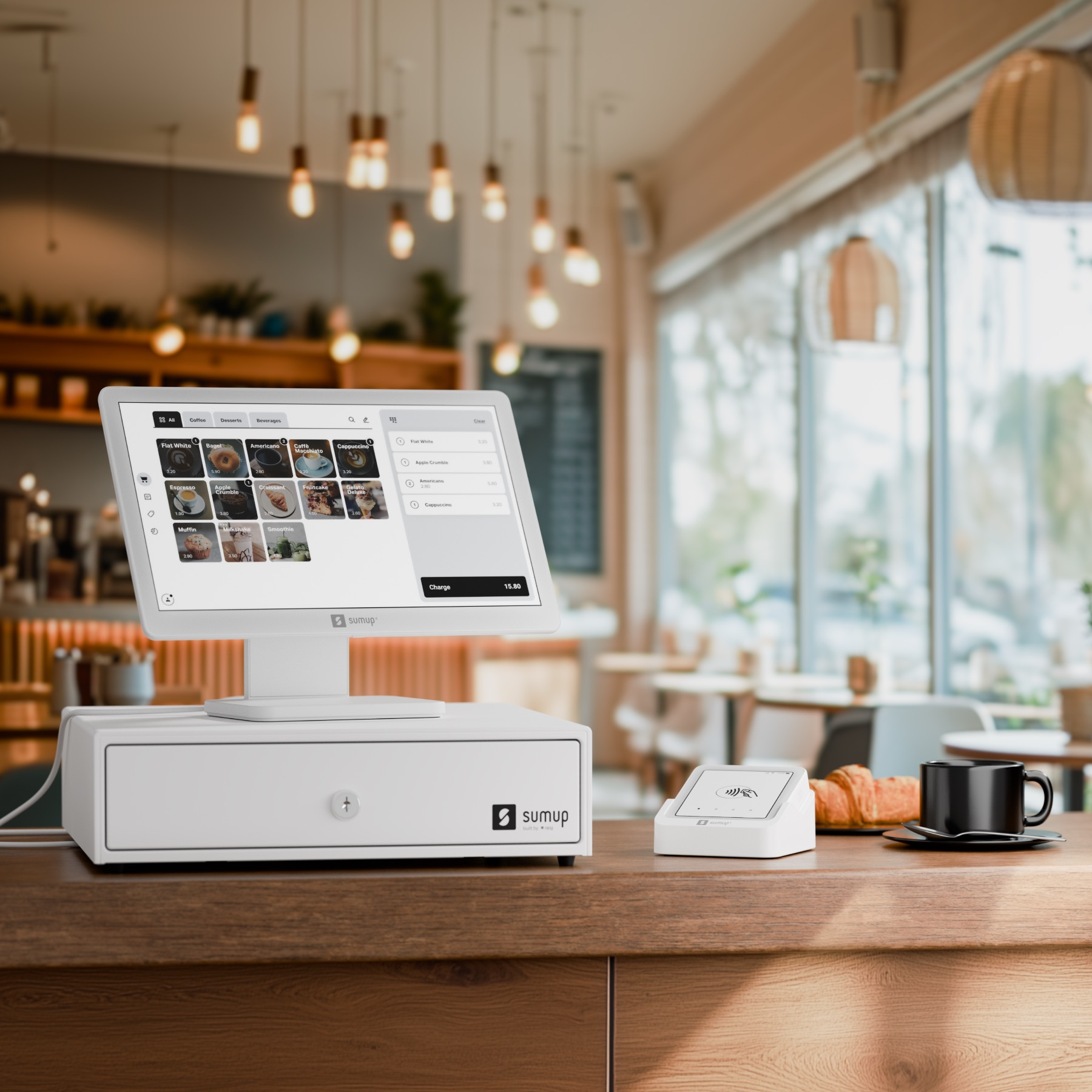 Un système de point de vente avec écran, tiroir, lecteur de cartes, café et pâtisserie sur un comptoir en bois.