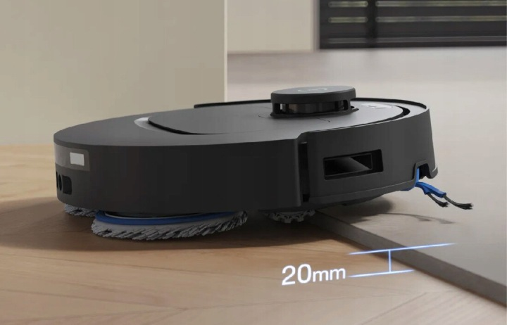 Czarny robot sprzątający z obrotowymi szczotkami pokonuje próg 20 mm.