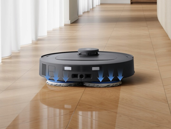 Ciemny robot odkurzający ze strzałkami skierowanymi w dół na drewnianej podłodze.