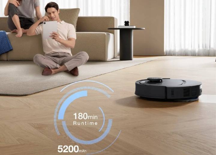 Mężczyzna siedzi na kanapie i używa tabletu, podczas gdy robot sprzątający czyści podłogę.
