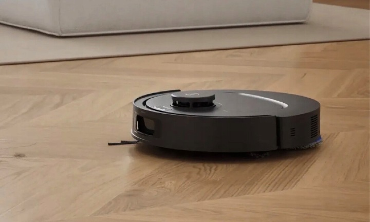 Ciemny robot sprzątający czyści drewnianą podłogę obok sofy.