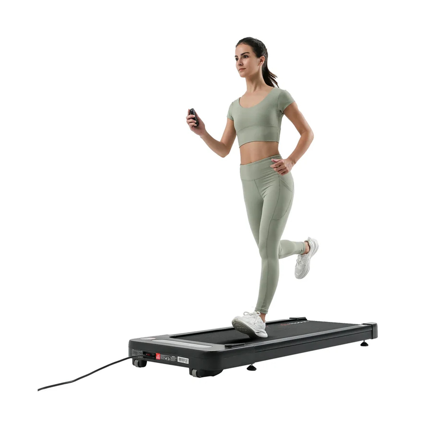 Una donna in completo sportivo verde menta corre su un tapis roulant tenendo un telecomando.