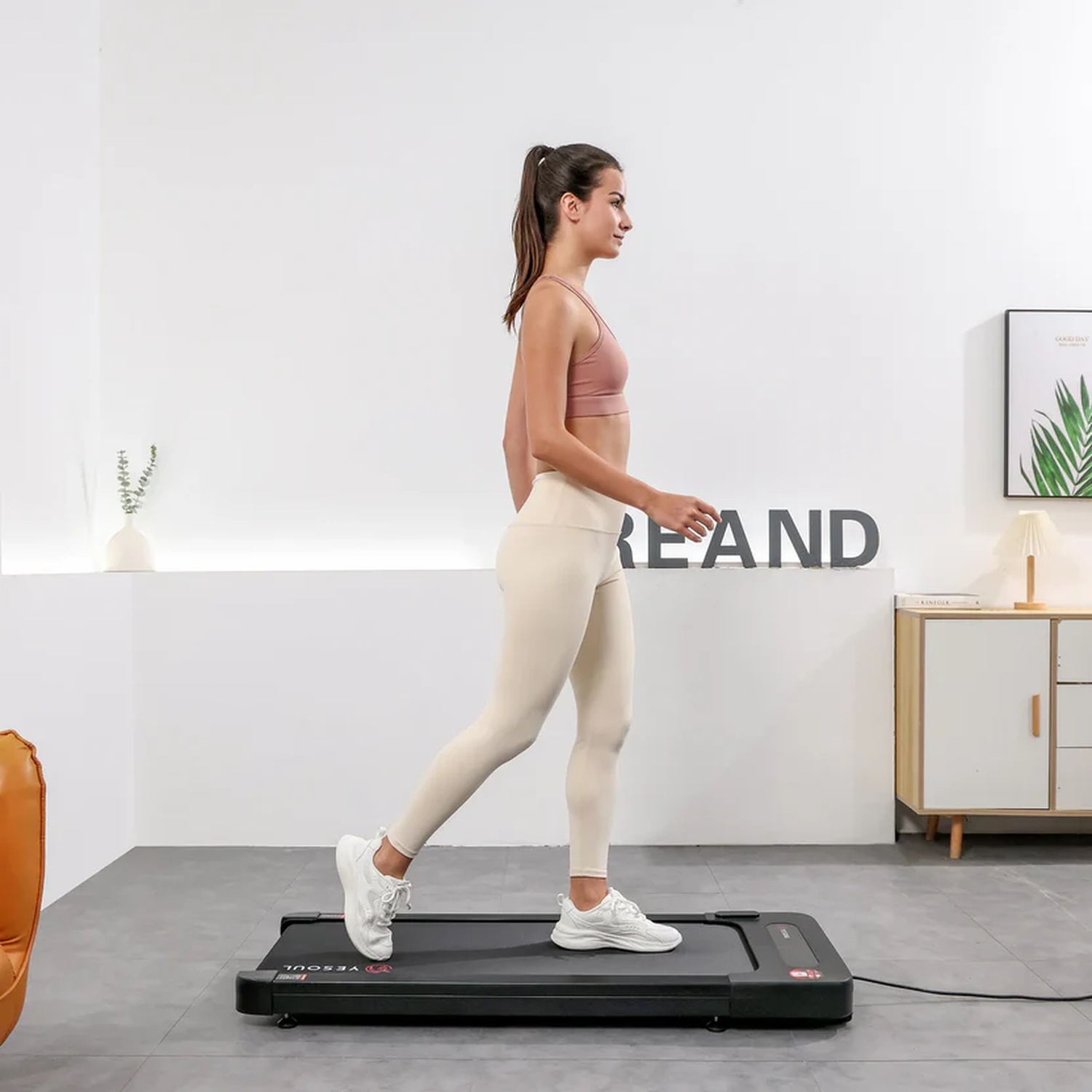 Una donna in abbigliamento sportivo cammina su un tapis roulant sottile in una stanza moderna.