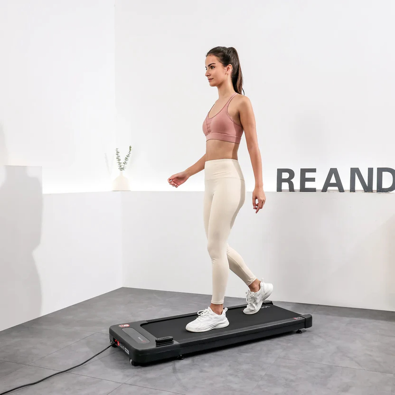 Una donna cammina su un tapis roulant. Indossa abbigliamento sportivo e scarpe da ginnastica bianche.