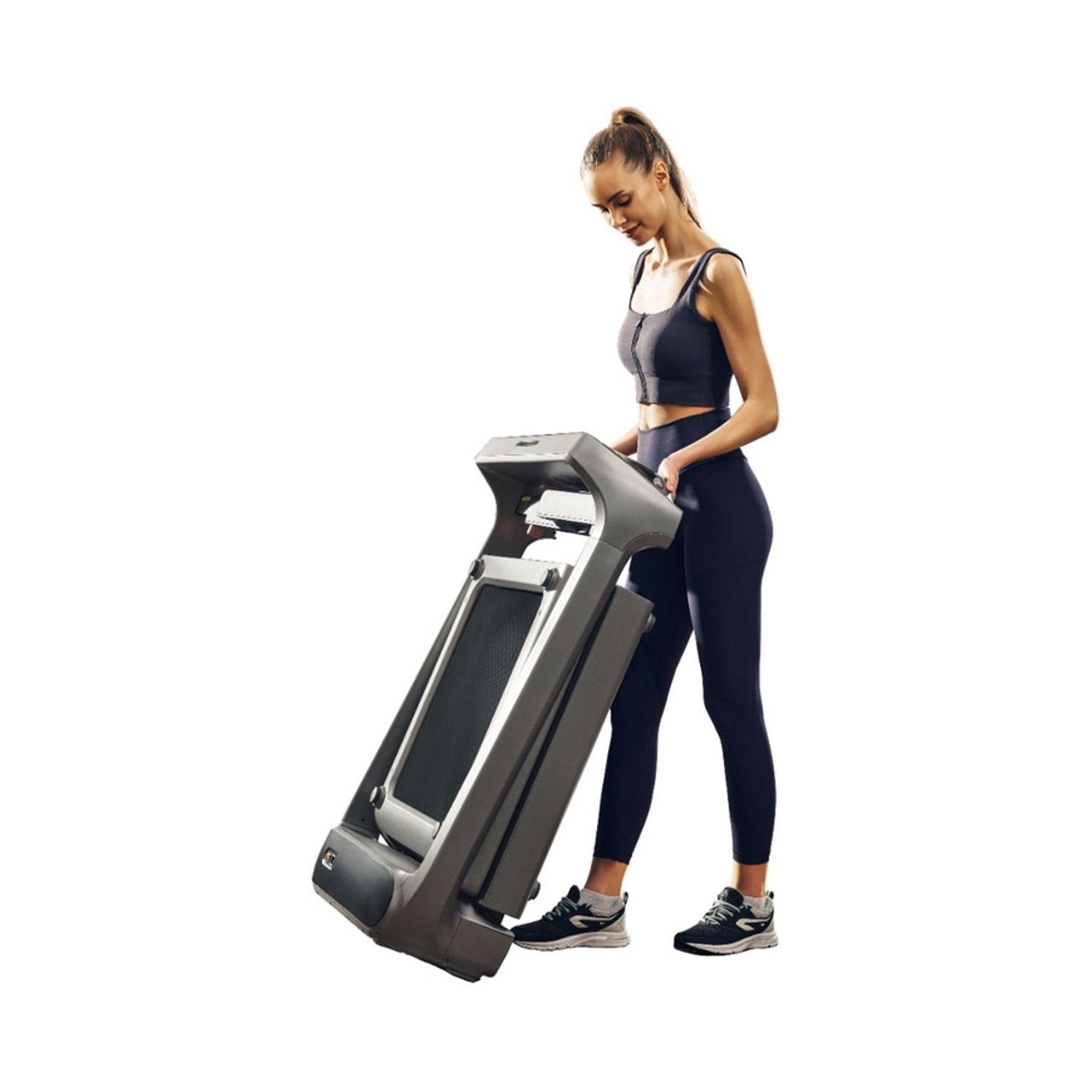 Donna in abbigliamento sportivo piega un tapis roulant grigio. Sfondo bianco.