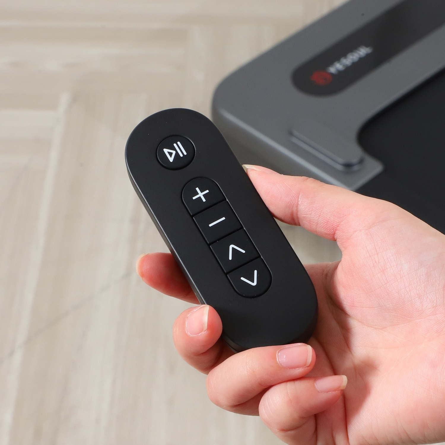 Una mano tiene un telecomando nero con pulsanti play/pausa, più, meno e frecce.