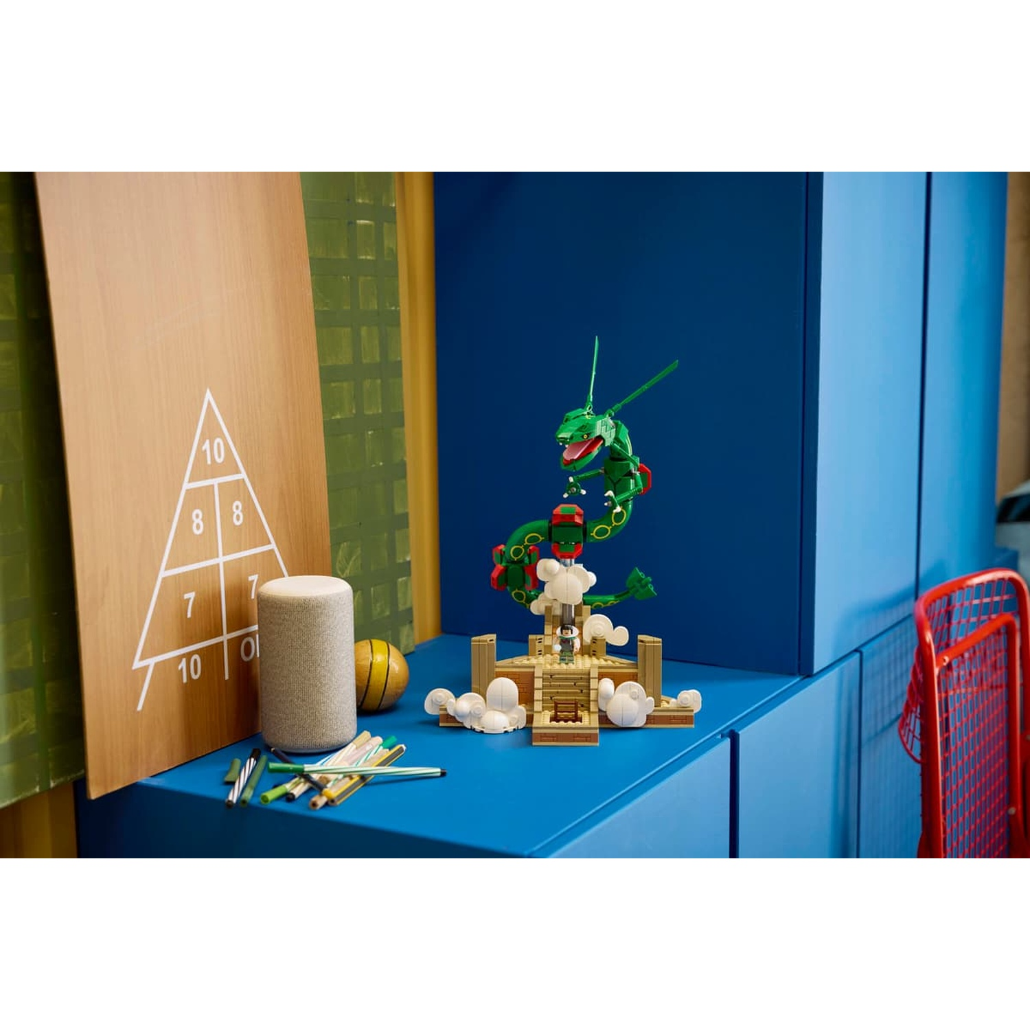 Modello Lego drago verde su superficie blu, con matite, altoparlante e tavola di legno.