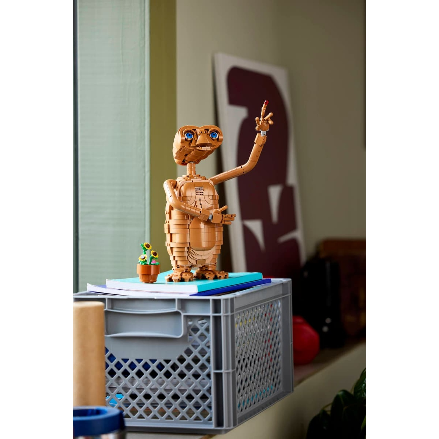 Una figura marrone Lego di E.T. con occhi blu sta su libri in cima a una cassa grigia.
