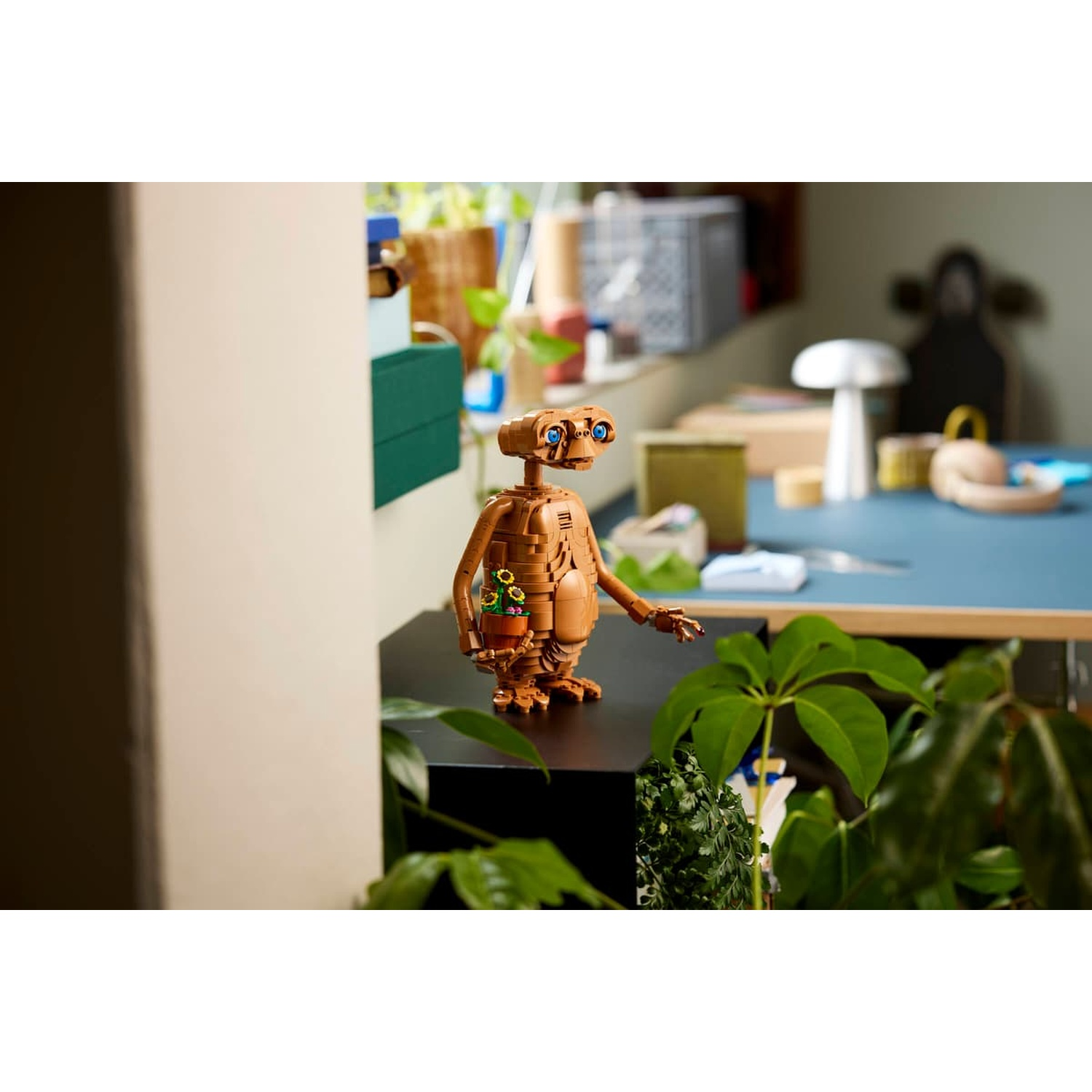 Una figura Lego di ET che tiene una pianta in vaso con girasoli si trova su una superficie nera.