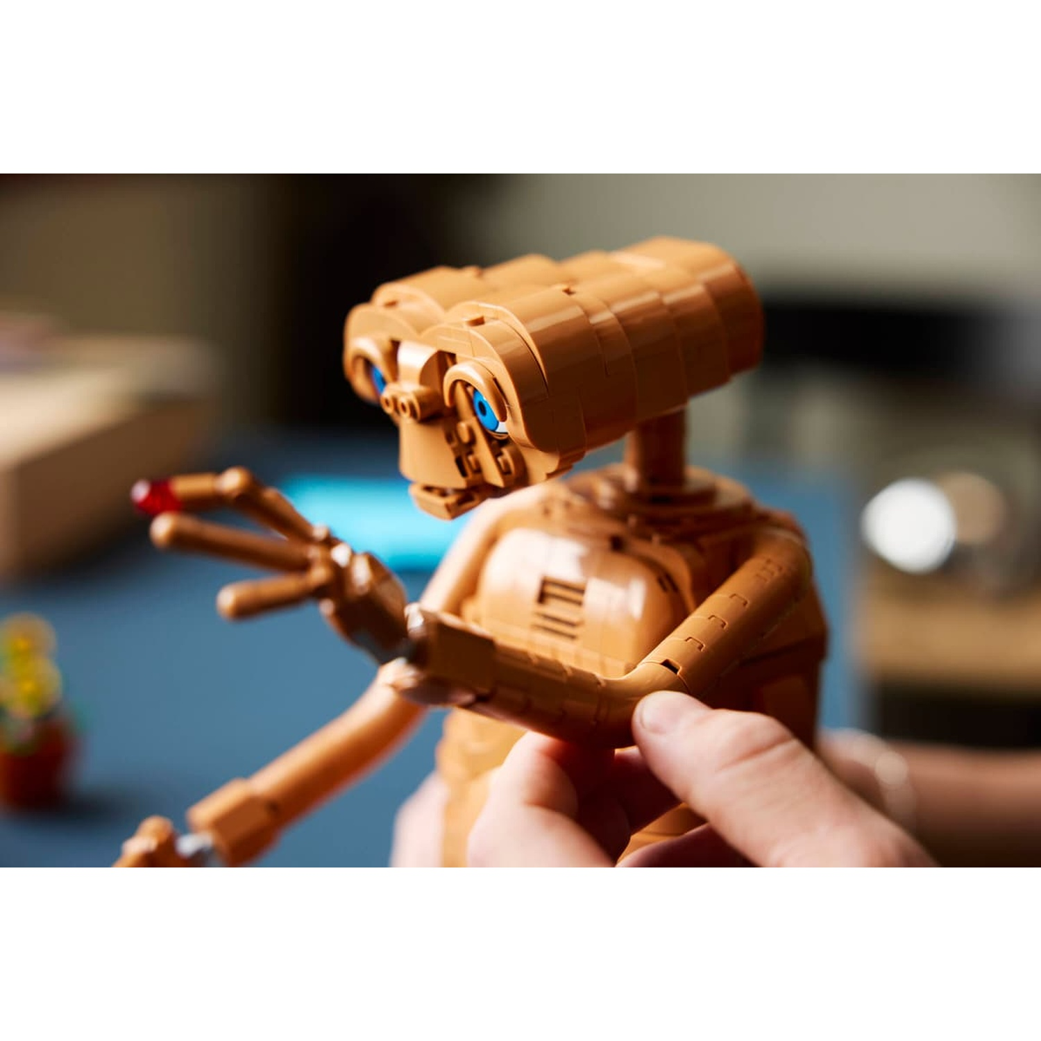 Una figura Lego marrone di ET con occhi blu è tenuta dalle mani.
