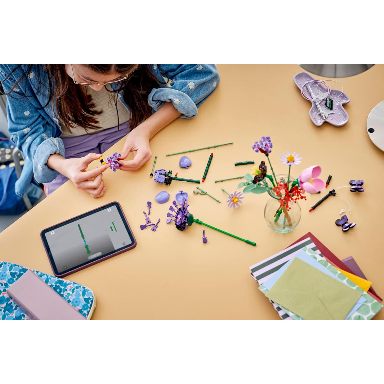 Una ragazza costruisce fiori Lego su un tavolo, con un tablet e lettere nelle vicinanze.