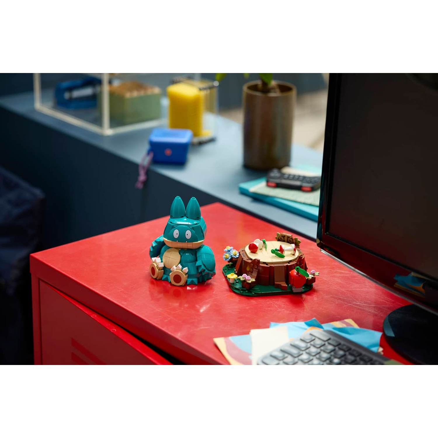 Un Pokémon Lego verde acqua siede accanto a un set di ceppi d'albero con bacche e fiori.