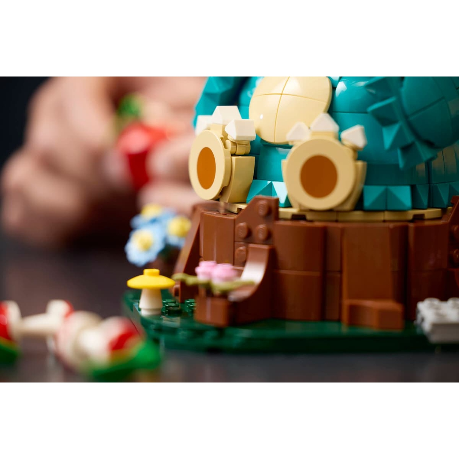 Modello Lego Snorlax con fiori e funghi, mano visibile sullo sfondo.