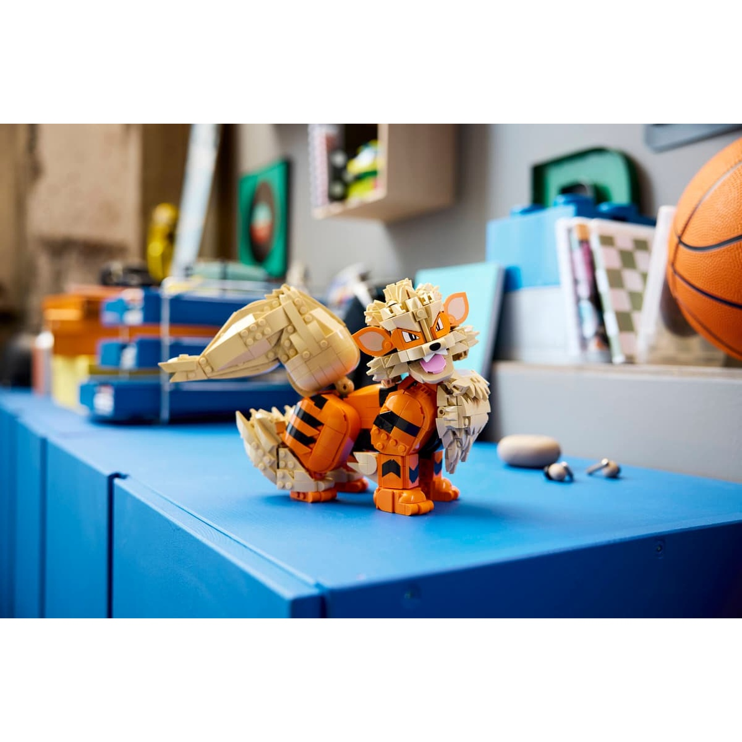 Un Arcanine LEGO su una superficie blu, con un pallone da basket e libri sullo sfondo.