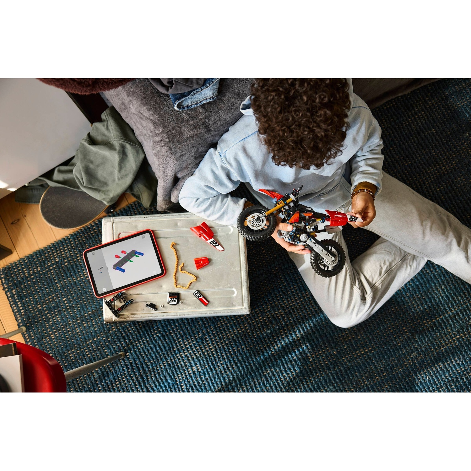Persona costruisce moto Lego, istruzioni su tablet. Pezzi su scatola metallo.