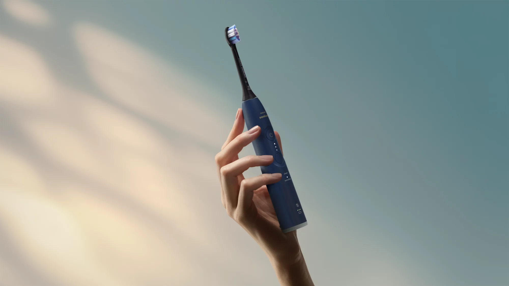 Eine Hand hält eine dunkelblaue elektrische Zahnbürste vor einem blauen Himmel.